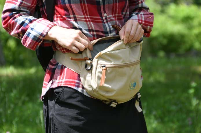 登山中にウエストバッグを開き、中身を取り出そうとしている場面